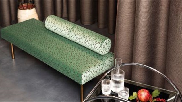 Grün bezogene Chaiselongue vor braunem Vorhang